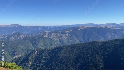 Wide panoramic view of vast mountain ranges, green forests, and ridges under a clear blue sky in Parang Mountains, Romania. Nature and travel video, 4K, 60fps.