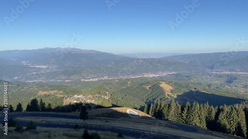 Panning shot of a winding mountain road, green valleys, and localities in Jiului Valley visible from Parang Mountains, Romania. Nature and travel video, 4K, 60fps.