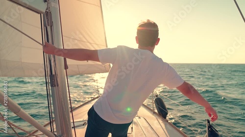 Yacht with sail gliding sea, cabin boy on deck gazing sun. Ships captain sailing ocean, raising hands. Sail towards your dream, adventure. Man sailing on yacht under white sail. Sea voyage free wind
