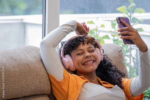 Canvastavla Smiling young woman relaxing on sofa at home, taking selfie on smartphone while
