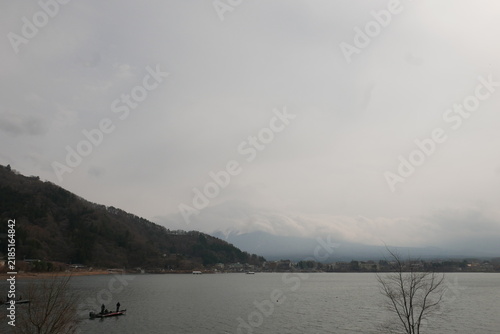 Foto Distant anglers fishing on lake beneath misty mountains