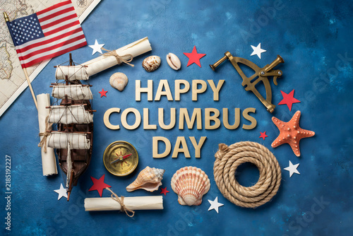 Flat lay composition of a model ship, sextant, compass, scrolls, seashells, and american flag on a blue textured background, for columbus day