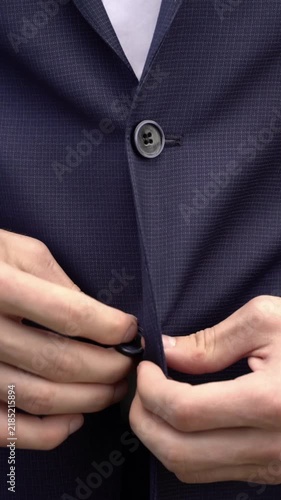 Close-up of a man buttoning a dark navy suit jacket over a white shirt. Hands fastening formal business attire. Professional menswear preparation.