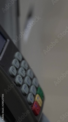 Woman paying for an item with a bank card on a POS terminal and taking the receipt. Close-up of female hand with purple nails pressing keypad buttons.