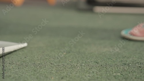 Close up view of green textured floor with occasional foot movements and objects like flip flops and tubes appearing. scene focuses on ground level details showing subtle changes
