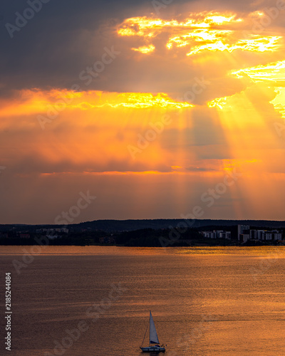 Bild auf Leinwand Vertical view of sailboat on lake under dramatic golden sunset crepuscular rays