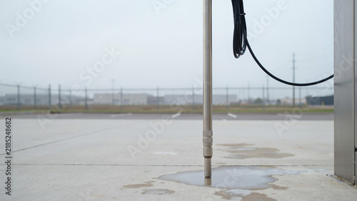 Metal pole with cable and puddle on concrete surface