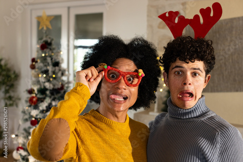 African American male friends posing, holding red glasses while wearing antlers at home