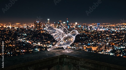 Transparent crystal bird sculpture on ledge against night city lights