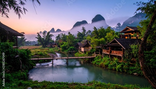 Traditional wooden village houses along a river with mist covered mountains in guilin china mountains landscape traditional
