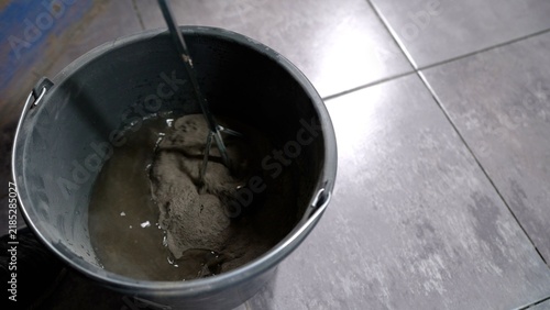 Fotografie Mixing tile adhesive cement powder with water in bucket using electric stirrer o