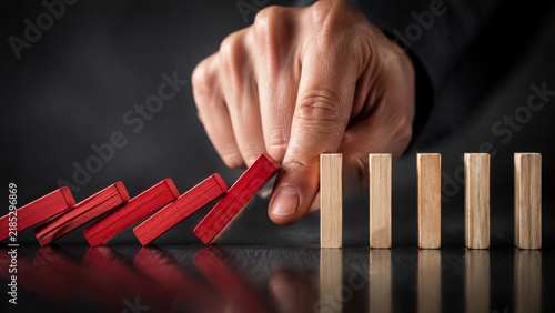 A human hand stopping a row of falling red dominoes to manage risk and control.