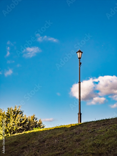 Minimalist outdoor street lamp post on a grassy hill under a bright blue sky with clouds
