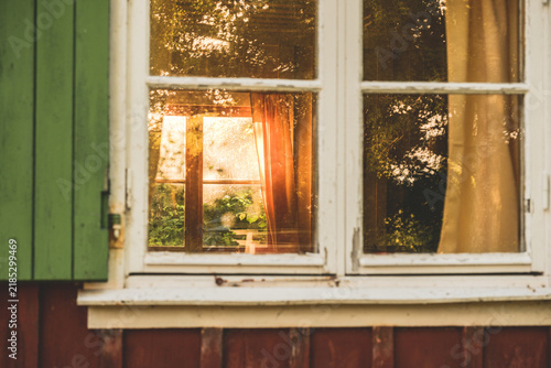 Old cottage window reflecting golden sunlight through curtains.