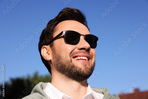 Handsome man in stylish sunglasses against blue sky, low angle view