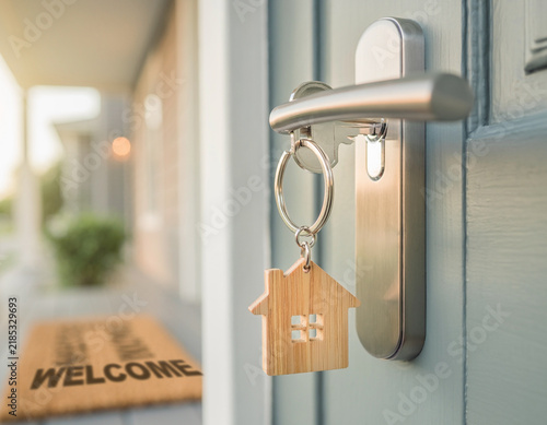 A house key with a wooden home keychain is inserted into a door for a new owner.