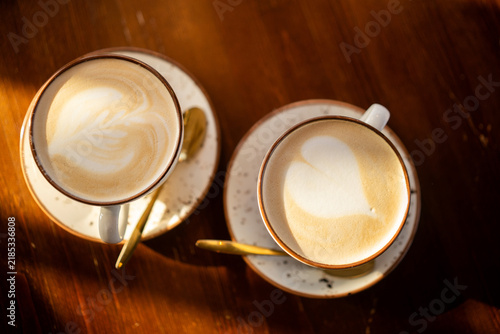 Two cappuccinos with latte art on wooden table in warm sunlight