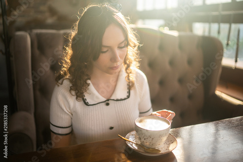 Woman drinking coffee in cafe with warm sunlight and sunglasses