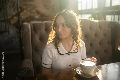 Woman drinking coffee in cafe with warm sunlight and sunglasses