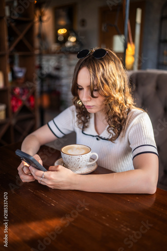 Young woman with curly hair using smartphone with coffee in cafe