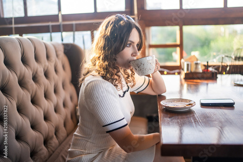 Woman drinking coffee in cafe with warm sunlight and sunglasses
