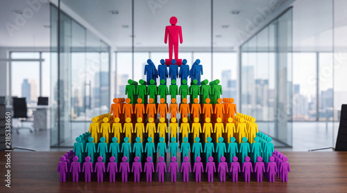 Obraz na płótnie Colorful human pyramid sculpture representing organizational hierarchy, leadership, and teamwork, with a single red figure at the apex in a modern office setting