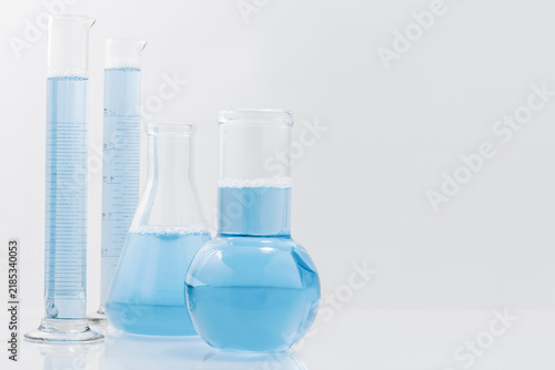 Laboratory flasks with blue liquid on light background and copy space