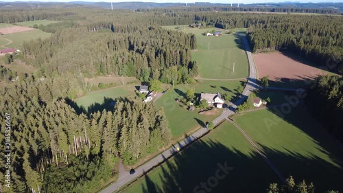 Drone flight over a vast green forest and surrounding rural countryside, with fields and distant landscape stretching toward the horizon on a bright sunny day.