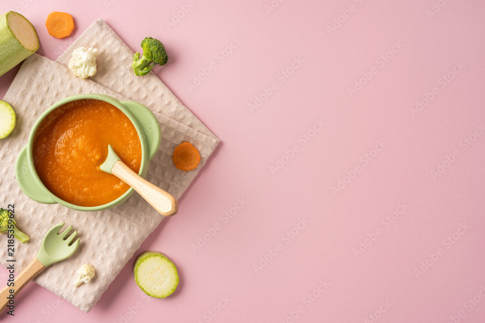 Obraz premium Baby's first feeding with healthy carrot puree in a green bowl on a pink background