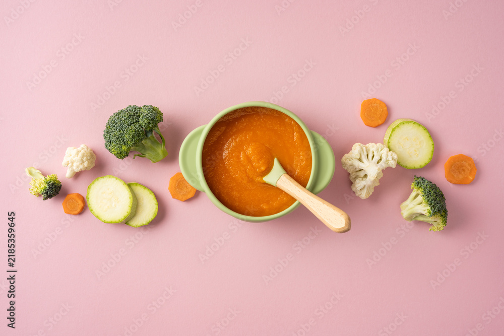 Obraz premium Baby's first feeding: homemade vegetable puree in a silicone bowl with wooden spoon on pink background