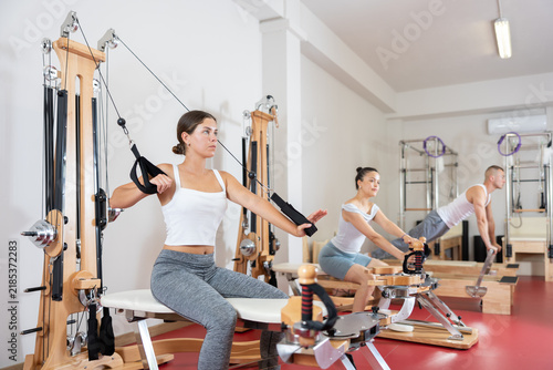 Sportive young girl training her arms pulling handle of cable exercise machine in fitness hall