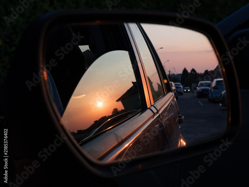 Golden sunset sky and sun reflected in a car side mirror during an evening road trip drive