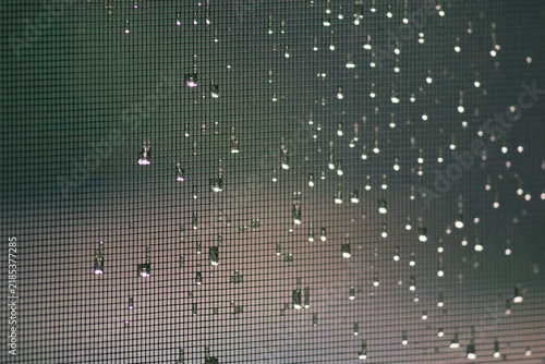 Raindrops and glowing bokeh lights on window screen mesh with green background