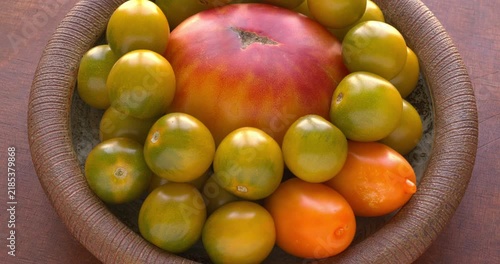 Old German, Green Grape Cherry, and Orange Banana tomatoes on a plate. Heirloom heritage tomatoes rotating on a brown ceramic dish. Wooden background. Table spin.