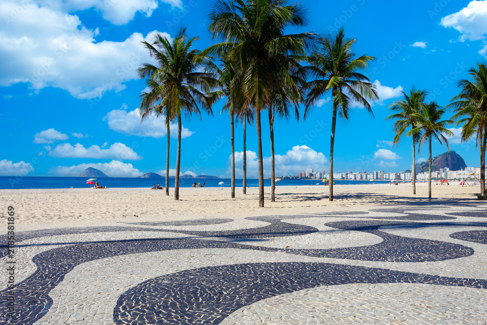 Obraz premium Iconic Copacabana beach boardwalk, palm trees, ocean, under a blue sky, Rio de Janeiro, Brazil. Sunny day travel scene.