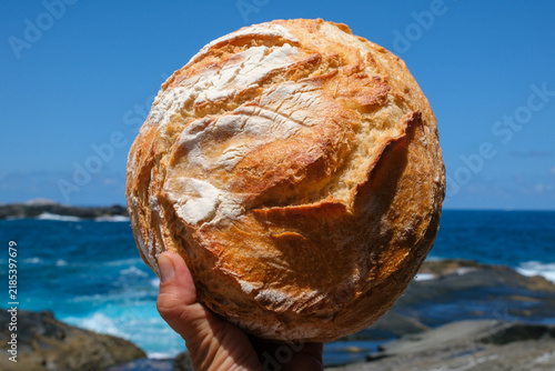 Rustic Artisan Bread Held by Hand Against a Blue Ocean