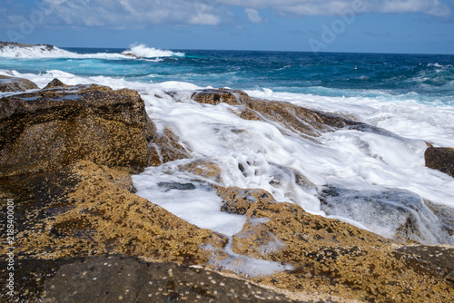 Ocean Foam Washing Over Rocky Shore on a Sunny Day