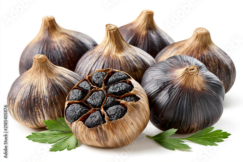 Black garlic bulbs displayed on a white surface with fresh herbs nearby