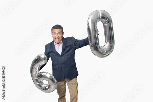 60-year-old Latino man with a dark skin displays 60 shaped balloons to celebrate his birthday and his entry into his old age