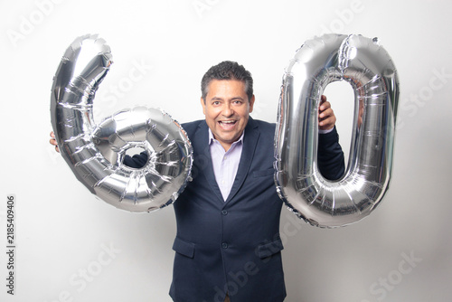 60-year-old Latino man with a dark skin displays 60 shaped balloons to celebrate his birthday and his entry into his old age