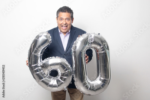 60-year-old Latino man with a dark skin displays 60 shaped balloons to celebrate his birthday and his entry into his old age