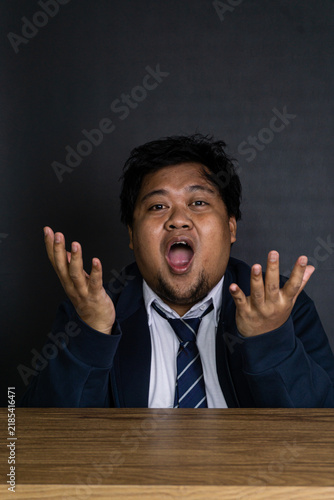 Canvastavla A frustrated young Asian male professional sits at a smooth wooden desk with raised open hands and a bewildered facial expression
