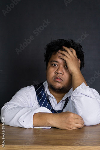 Photography A thoroughly drained young Asian male professional sits slumped at a clean woode