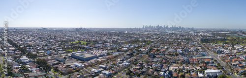 Wide panoramic aerial view sweeping over the suburban residential grid of Yarraville and the inner west, looking east toward the distant city skyline. Melbourne, Victoria, Australia