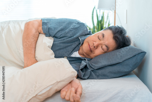 Naklejka 自宅のベッドで眠る60代から70代のシニア男性。睡眠と健康、快眠をイメージした寝室での生活