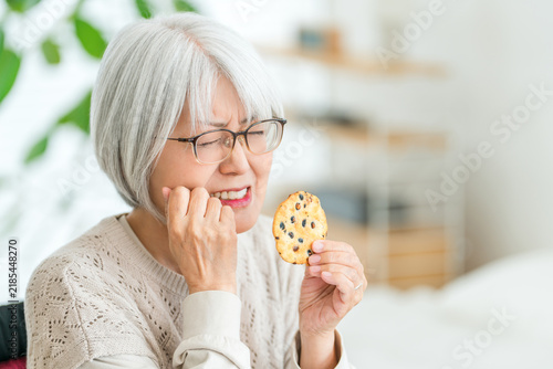 Plakat 硬いせんべいを食べて歯の痛みに悩むシニア女性。噛みにくさを感じる高齢者