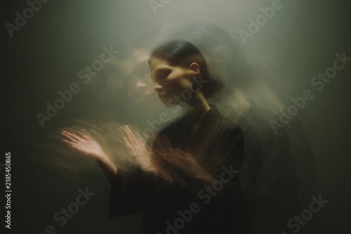 Shadow ritual portrait of a shaman woman breathing to animate her own shadow with motion blur for moody background and performance imagery