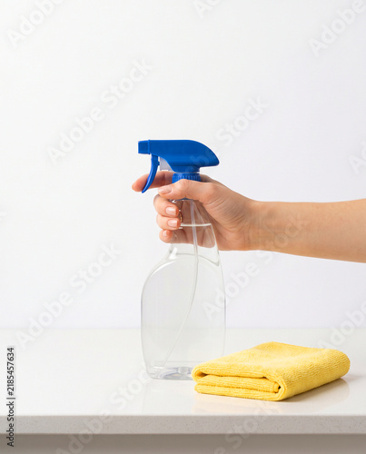 Hand Holding Spray Bottle near Yellow Microfiber Cloth on Counter
