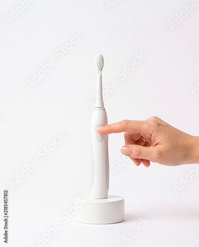 Hand Pressing Power Button on White Electric Toothbrush on Podium
