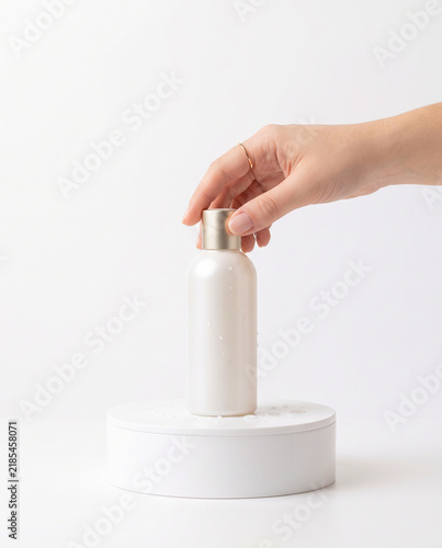 Hand Touching Pearl White Cosmetic Bottle on White Podium Mockup
